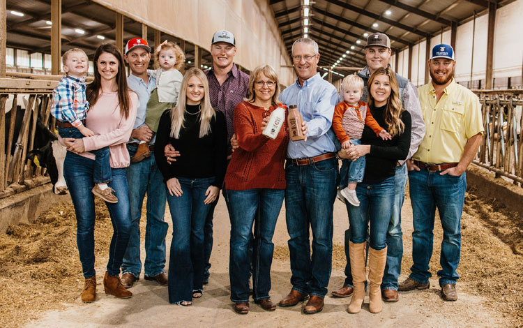 Una familia de granjeros lecheros posa para una foto grupal, y la edad de las personas varía desde niños pequeños hasta ancianos.
